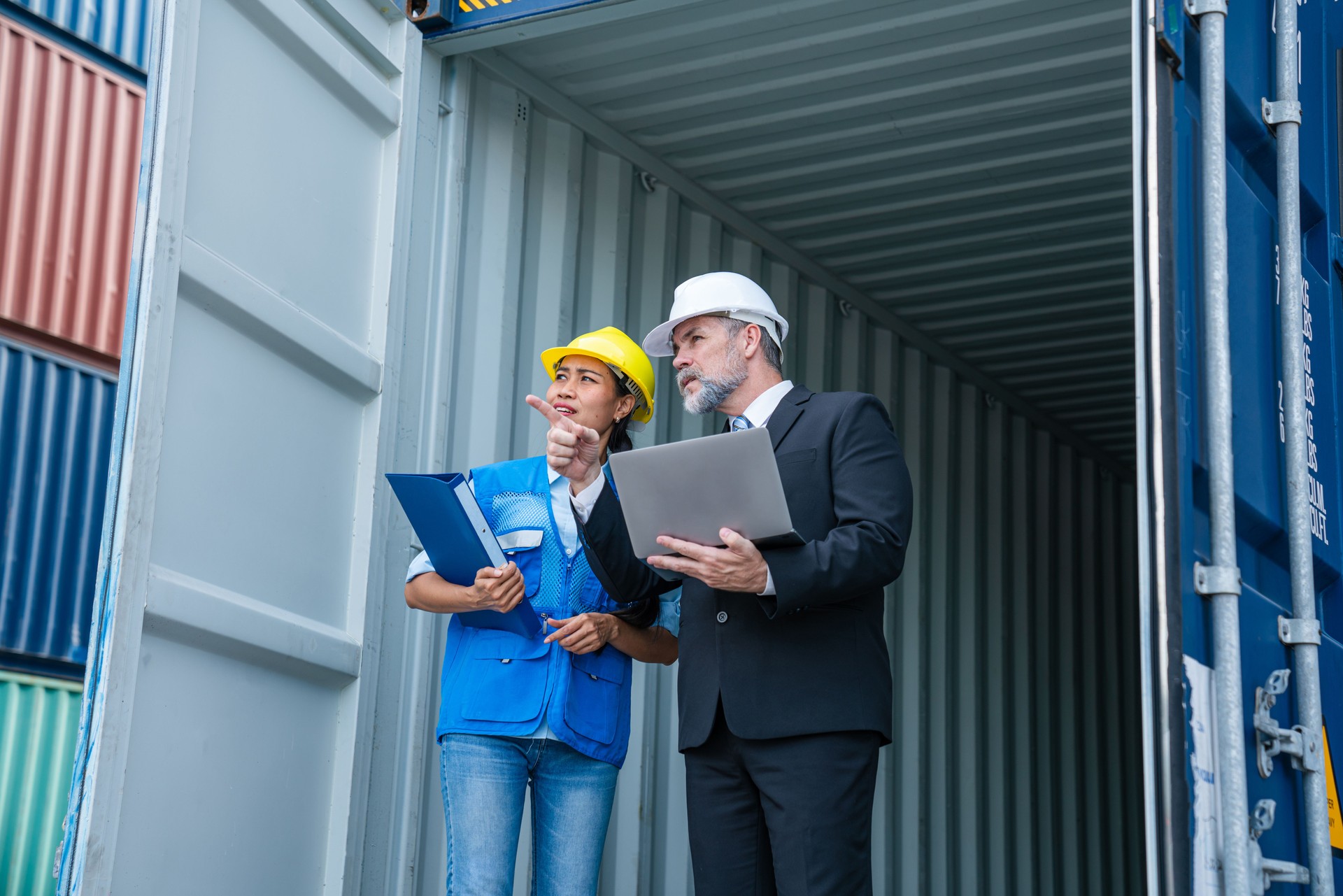 Container yard manager with safety hat talking to foreman about the goods inside the warehouse.